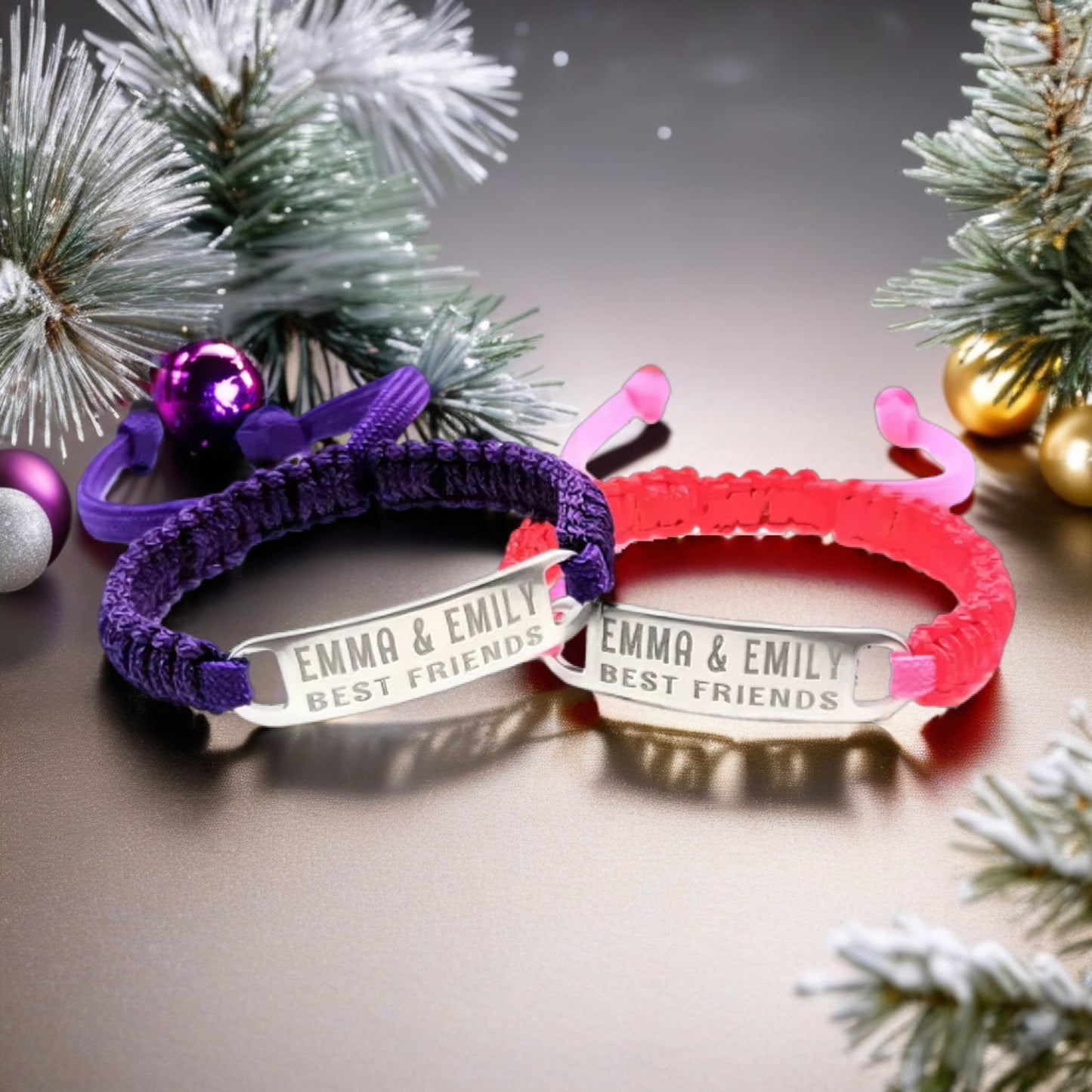 Two adjustable micro paracord bracelets with engraved tags displaying Emma & Emily Best Friends, set against a festive background with pine branches and ornaments. One bracelet is purple, and the other is pink.