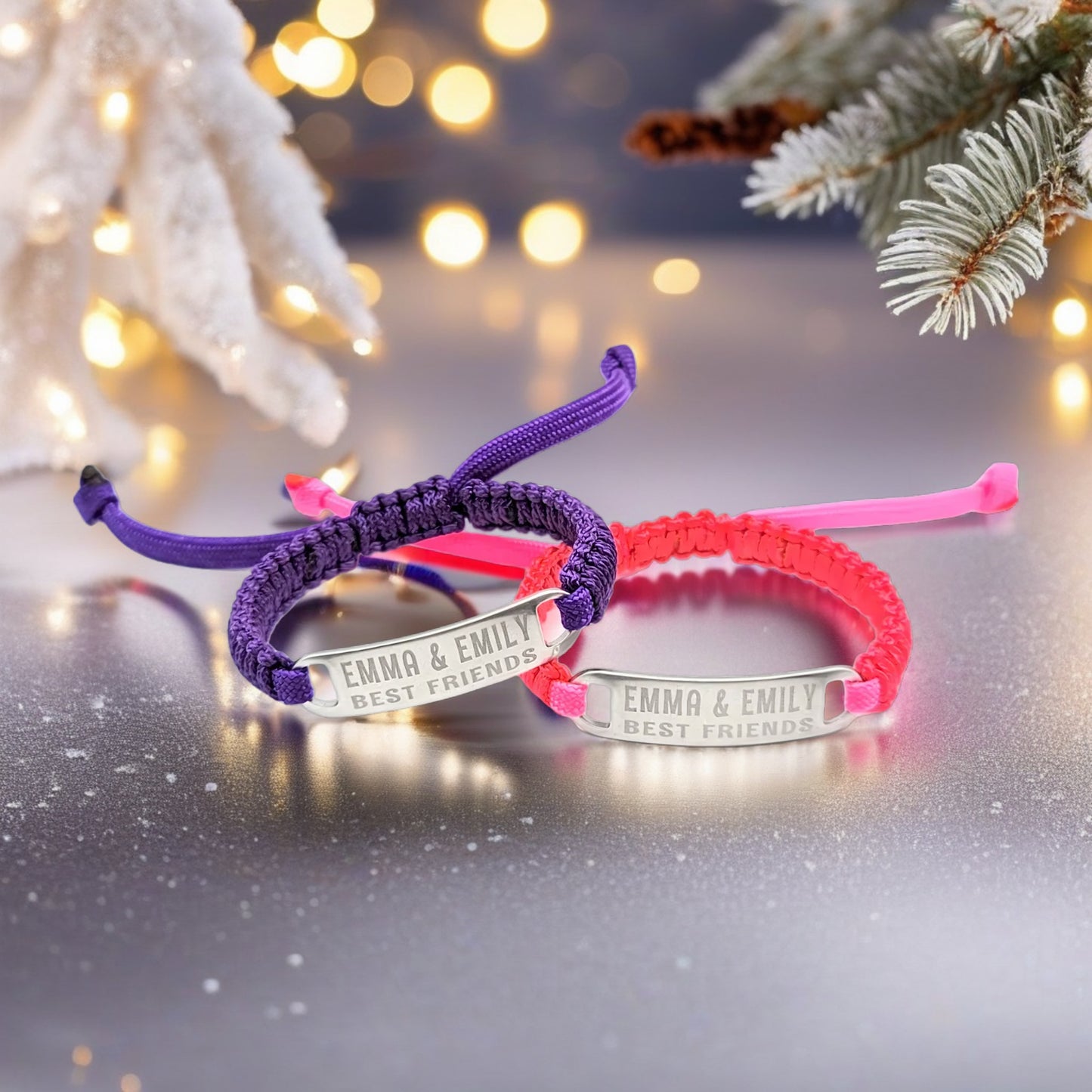 A woman's wrist wearing both the purple and pink adjustable best friends bracelets, engraved with Emma & Emily Best Friends, shown in a winter-themed setting with pine branches.