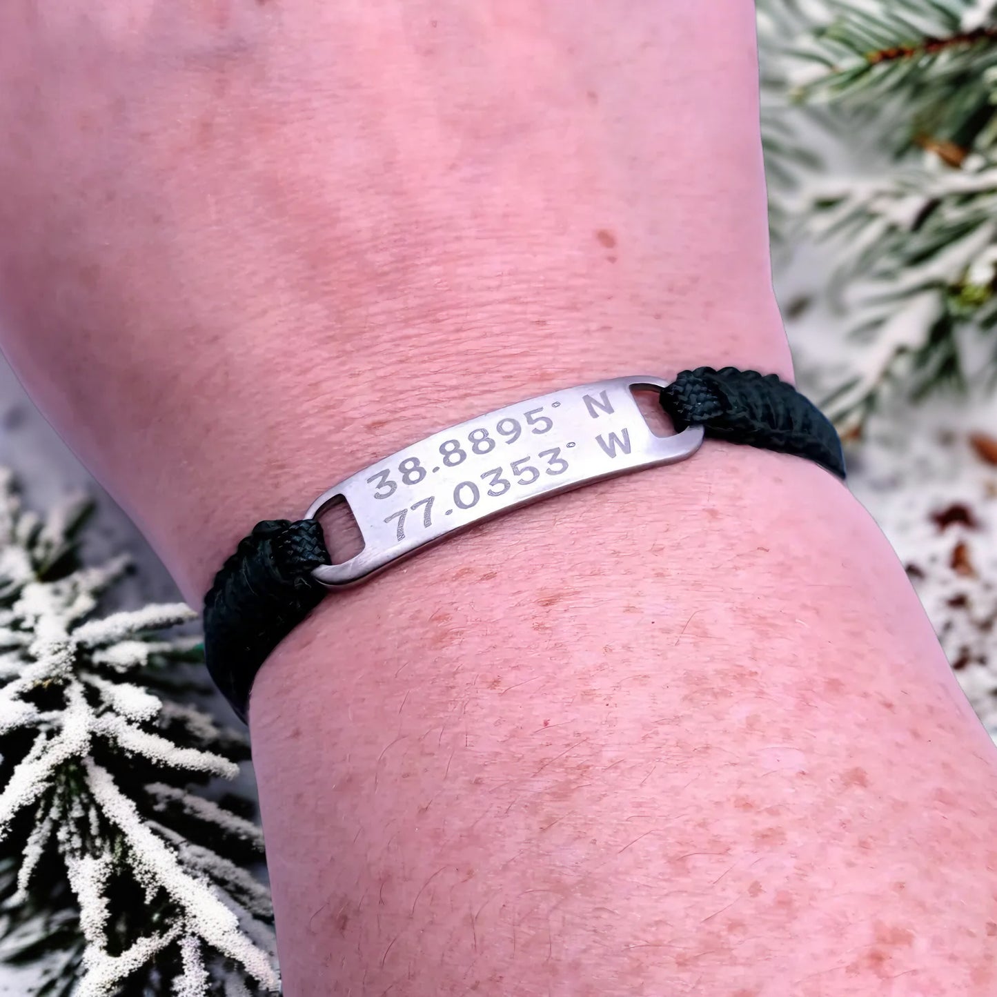 The bracelet worn on a person’s wrist, with a clear view of the engraved tag against a backdrop of frosted greenery.