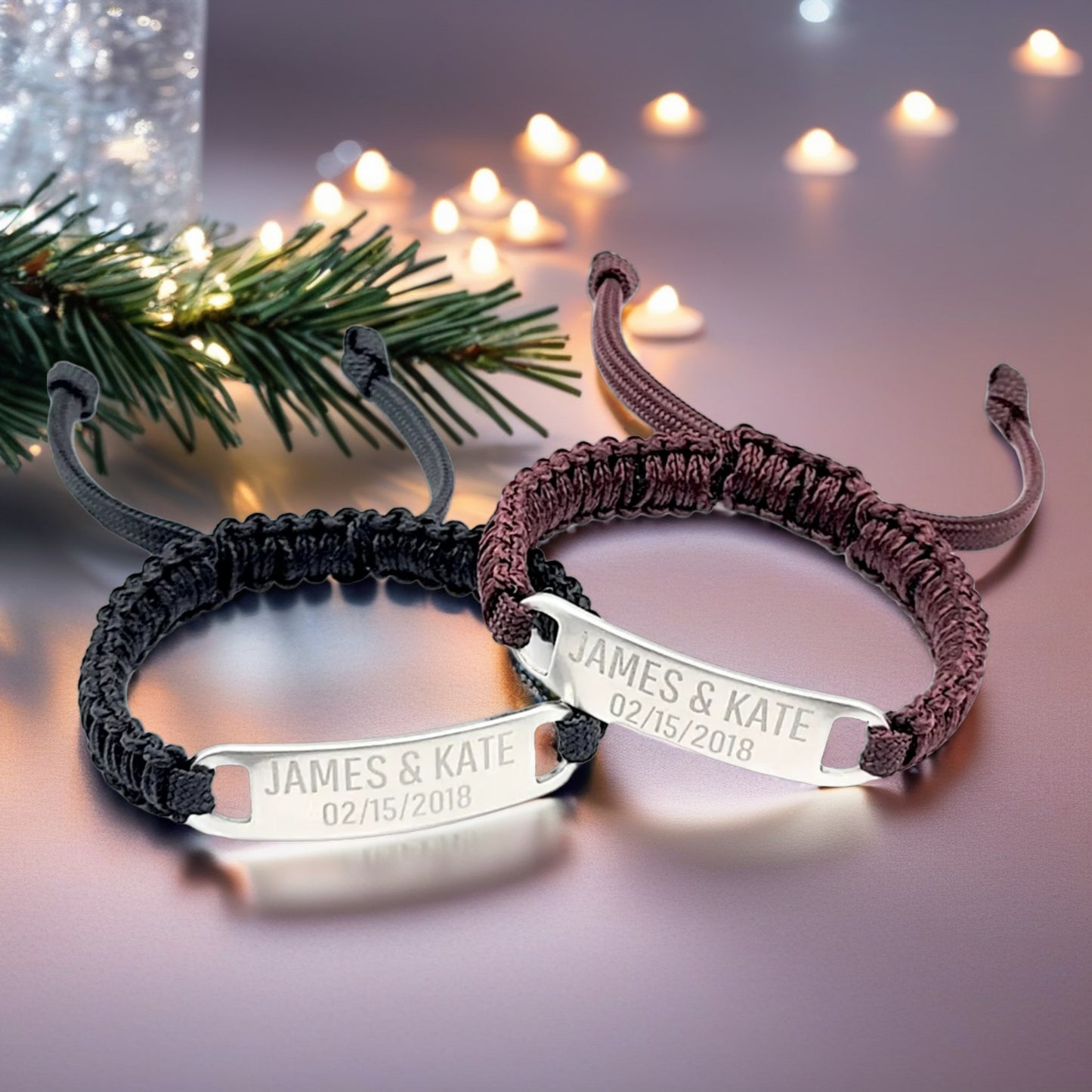 Two matching micro paracord bracelets displayed in a cozy, festive setting with holiday lights in the background. The engraved stainless steel plates read James & Kate 02/15/2018, emphasizing the personalized detail.
