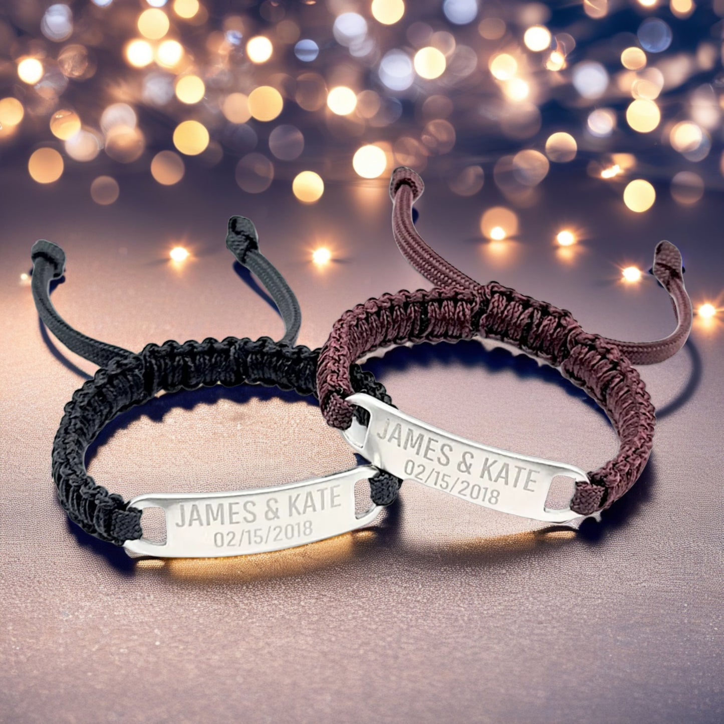A festive-themed image featuring two adjustable micro paracord bracelets, maroon and black, with engraved tags displaying "James & Kate 02/15/2018." The bracelets are set against a sparkling background with bokeh lights for an elegant, romantic feel.