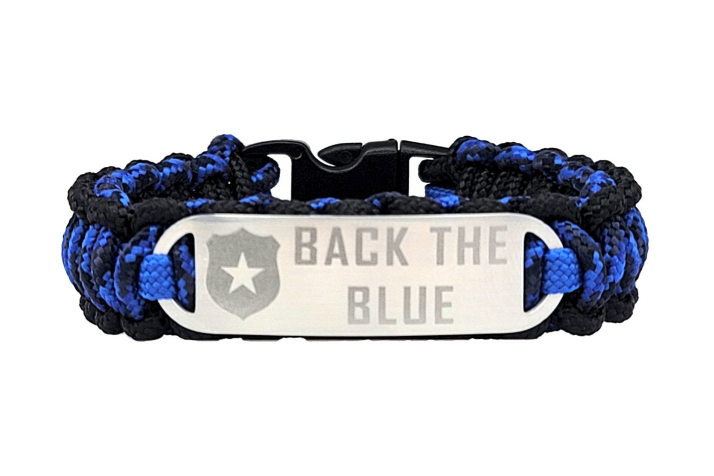 Blue & Black thin 275 paracord ID bracelet with a silver, stainless steel ID tag engraved Back the Blue and a police badge symbol, displayed on a smooth surface with police vehicles in the background.