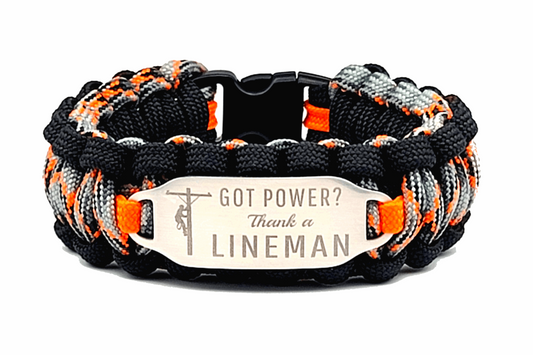 An Orange, black, and grey paracord ID bracelet with a silver, stainless steel ID tag engraved with Got Power?  Thank a Lineman and a Lineman silhouette, displayed on a white background.