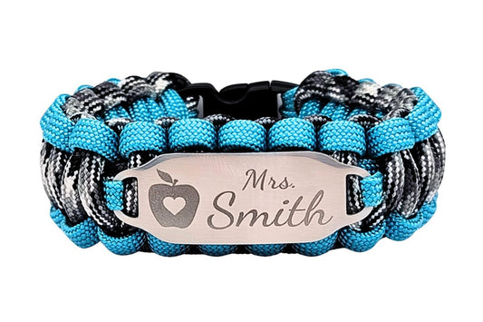 Grey, white, black, and teal paracord ID bracelet with a silver, stainless steel ID tag engraved with the name Mrs. Smith and an apple silhouette, displayed on an all white background.