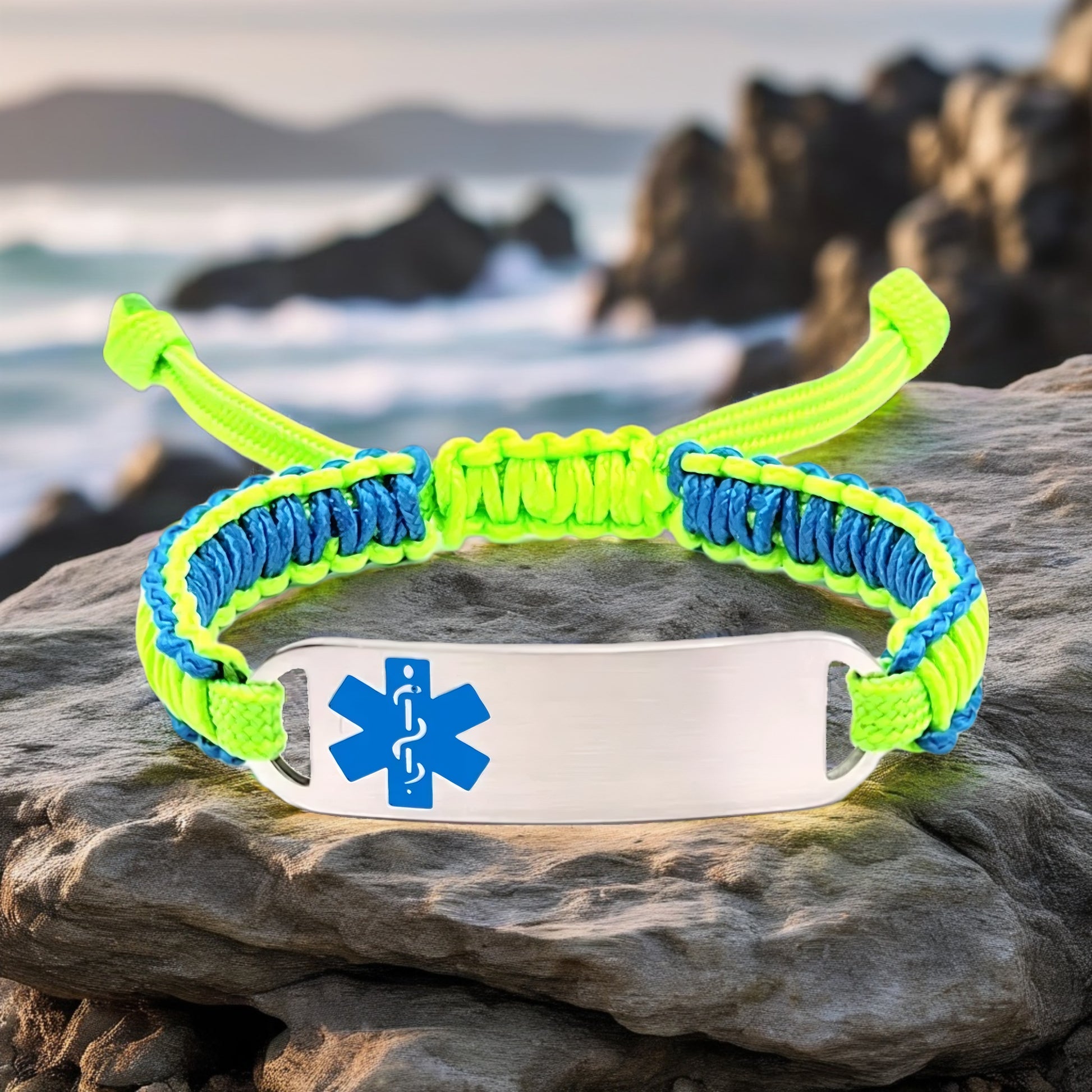 Adjustable micro paracord medical ID bracelet on a rock with an ocean backdrop. Features neon green and blue cords with a polished silver tag engraved with a blue medical alert symbol, offering a bold and functional design.